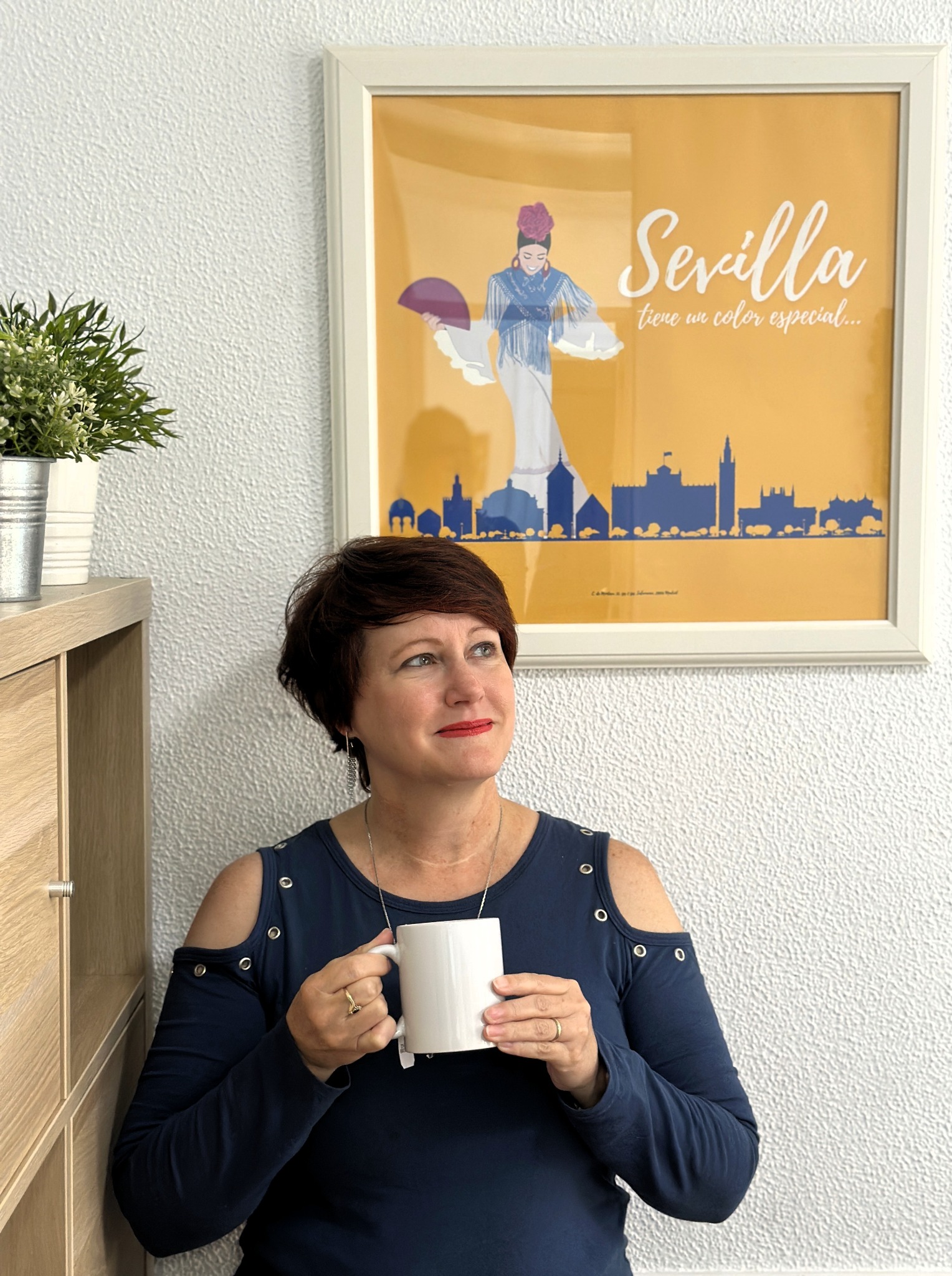 Adrienne holding a mug beside a colorful Sevilla print